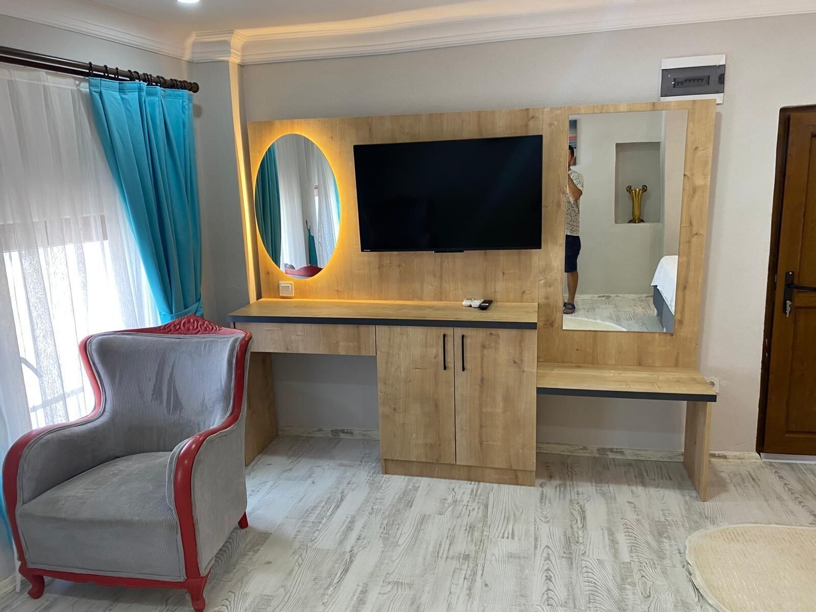 A modern room with a wooden desk, a flat-screen TV, a mirror, and a red and grey armchair.