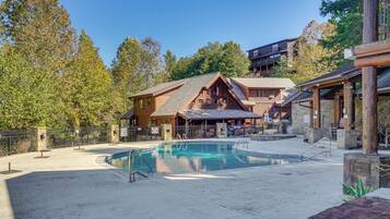 A wooden lodge with a pool, surrounded by trees and a clear sky.