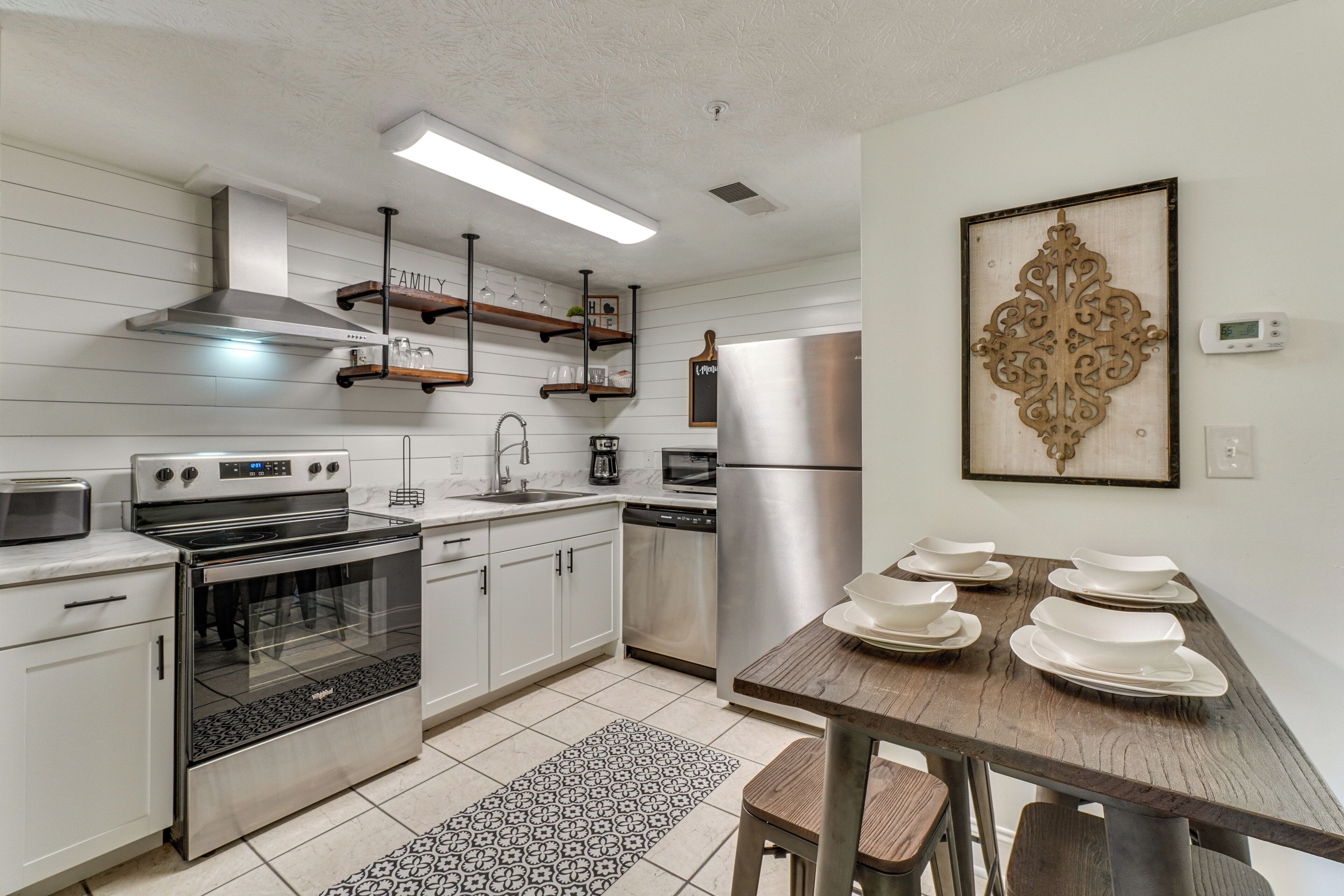 A modern kitchen with stainless steel appliances, wooden shelves, and a dining table set with white plates.