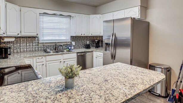 A modern kitchen with white cabinets, stainless steel appliances, and a granite countertop. - 3 Mi to Texas Tech: Cozy Home w/ Private Yard! (Lubbock)