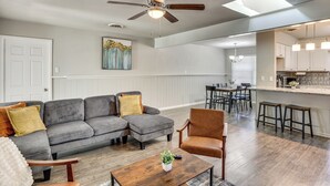A modern living room with a sectional sofa, a coffee table, and a dining area with a kitchen in the background. - 3 Mi to Texas Tech: Cozy Home w/ Private Yard! (Lubbock)