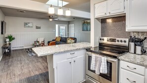 A modern kitchen with white cabinetry, a granite countertop, stainless steel appliances, and a dining area with a gray sofa and a coffee table. - 3 Mi to Texas Tech: Cozy Home w/ Private Yard! (Lubbock)