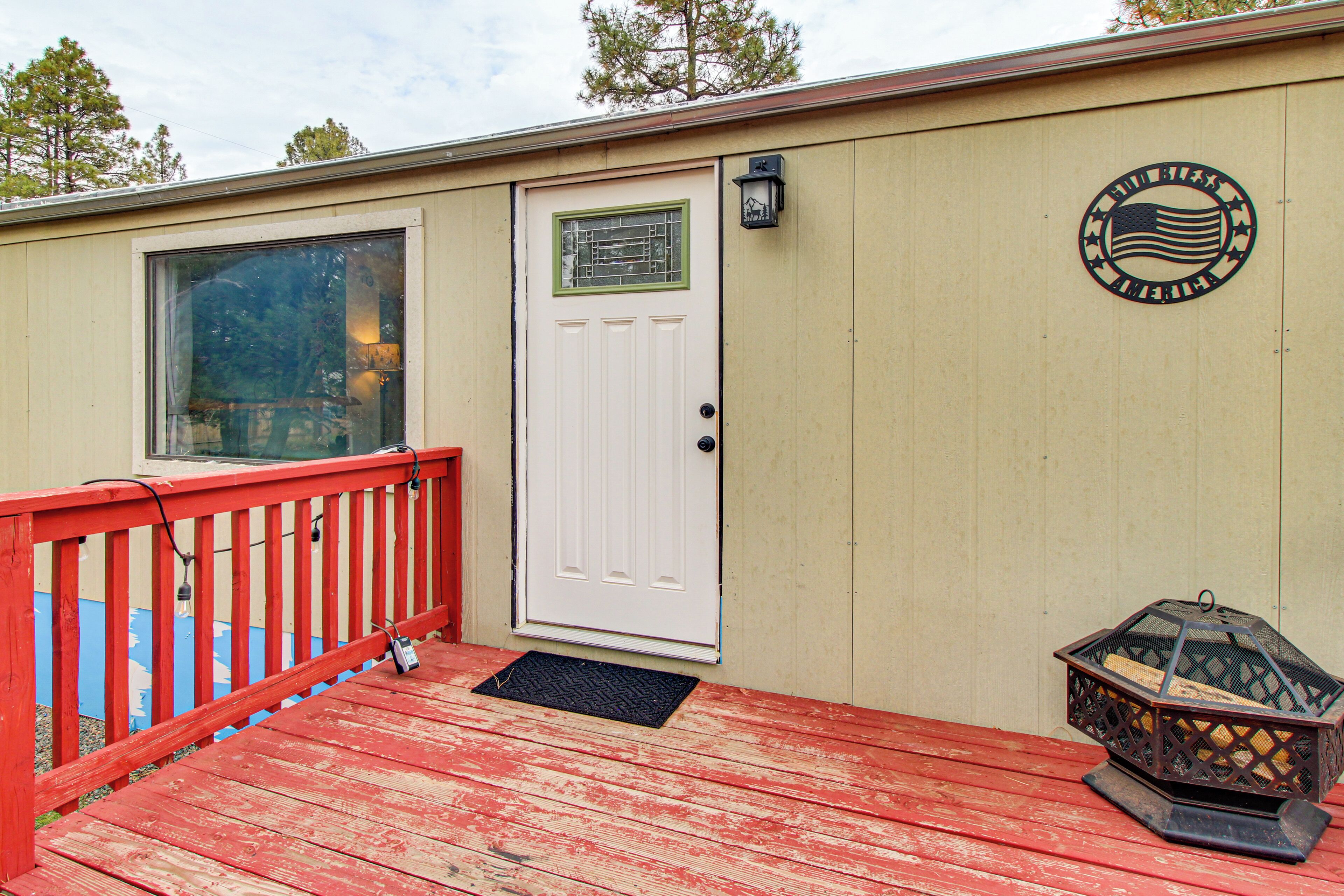 A wooden deck with a red railing, a white door, and a small outdoor lamp.