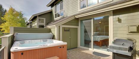 A backyard with a hot tub, a grill, and a covered patio area.