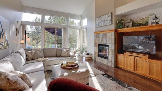 A modern living room with a sectional sofa, a fireplace, a large TV, and large windows offering a view of the outdoors.
