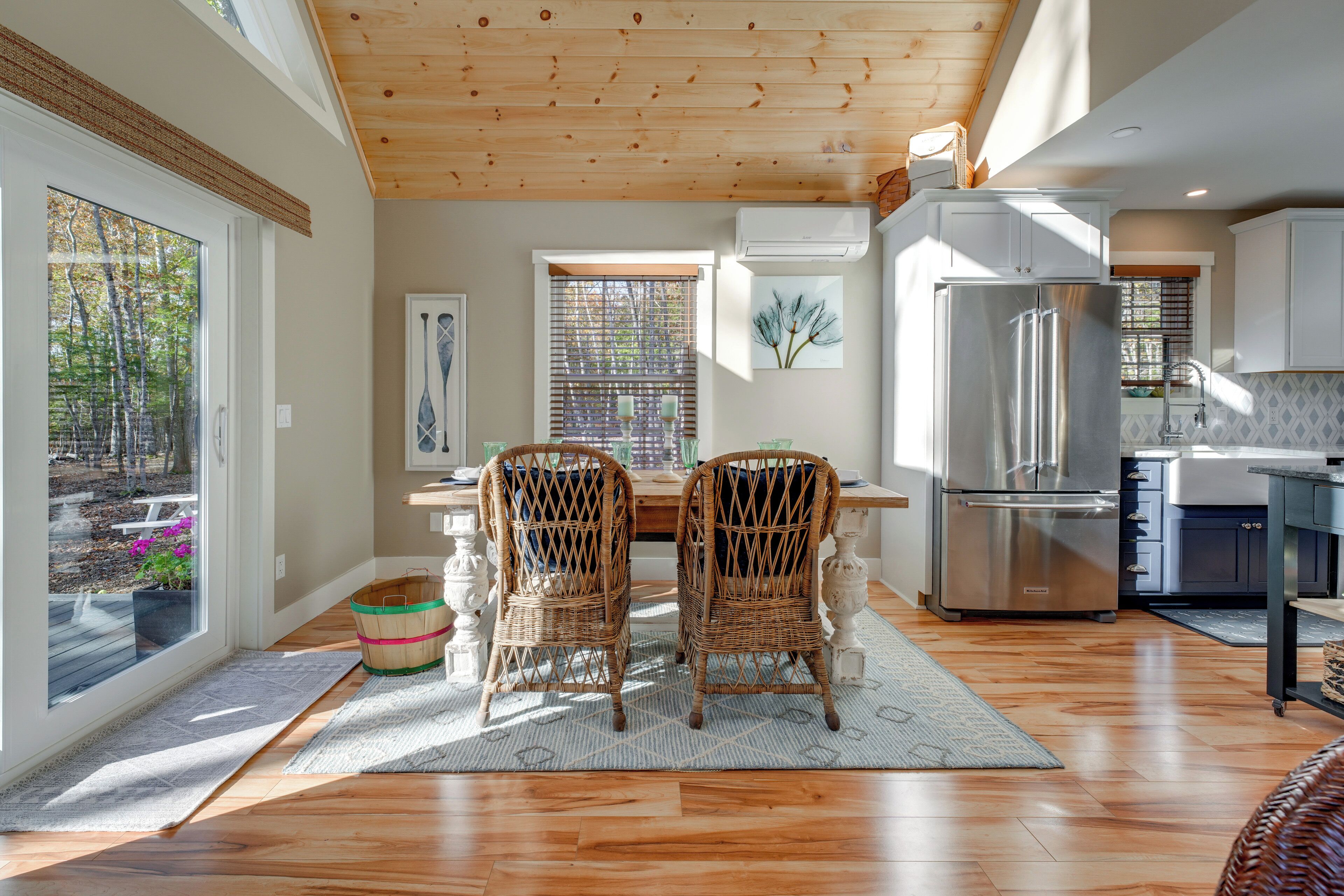 A modern kitchen with wooden flooring, a stainless steel refrigerator, and wicker chairs.