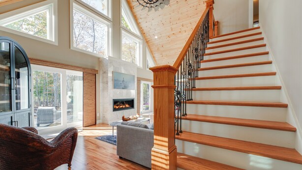 A spacious living room with a wooden staircase, large windows, and a fireplace. - 'valhalla': Family Home on Frye Island w/ Golf! (Raymond)