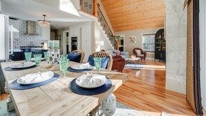 A spacious dining area with a wooden table set for a meal, a staircase leading to an upper level, and a view of the living room in the background. - 'valhalla': Family Home on Frye Island w/ Golf! (Raymond)