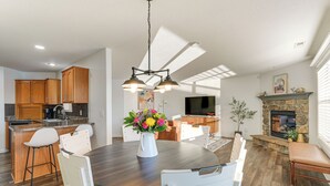 A modern kitchen with wooden cabinets, a dining area with a round table and white chairs, and a stone fireplace.