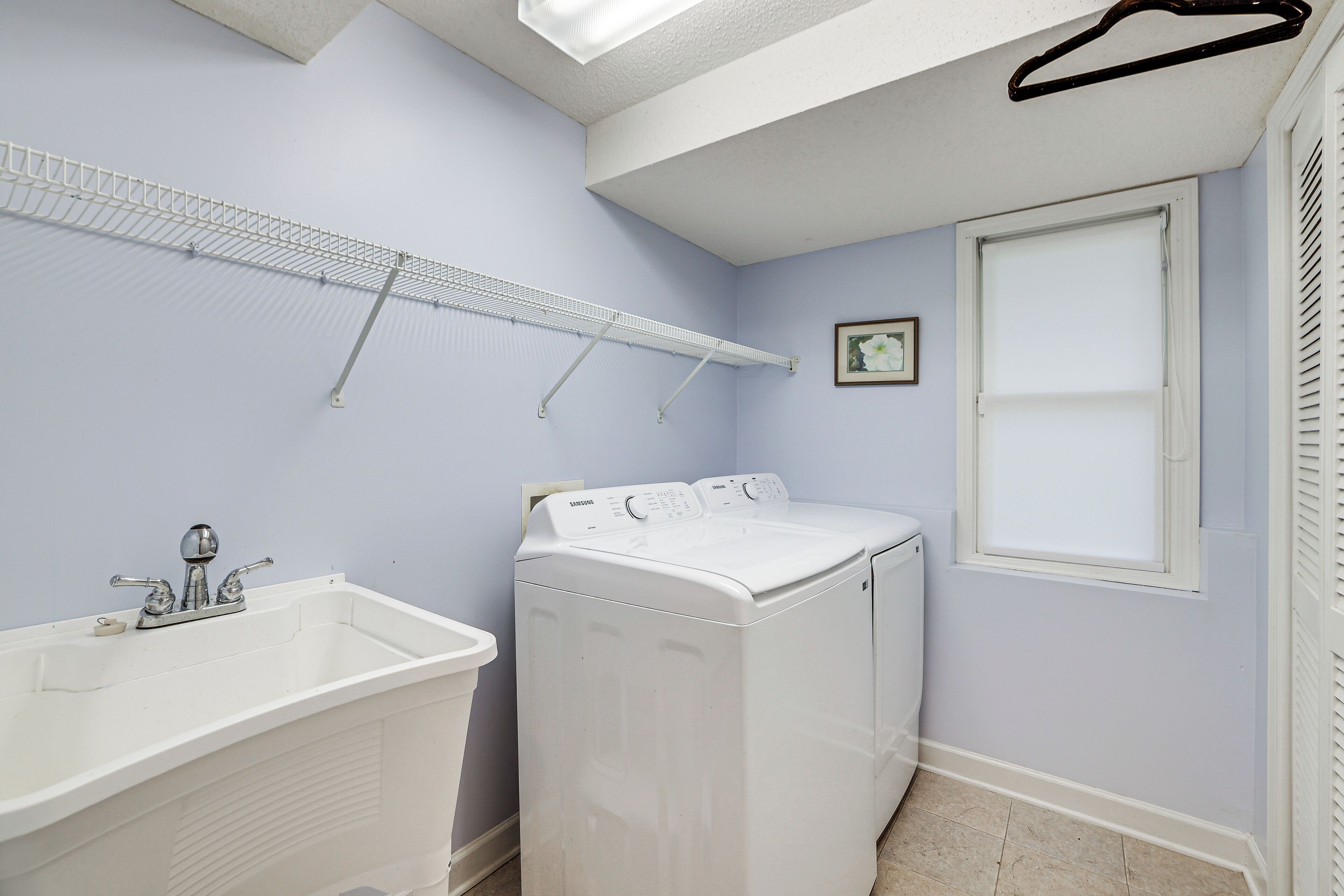 A laundry room with a washing machine, a sink, and a drying rack.