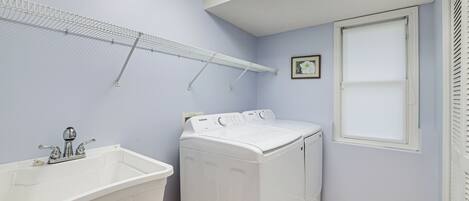 A laundry room with a washing machine, a sink, and a drying rack.