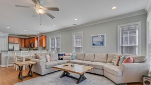 A spacious living room with a sectional sofa, a wooden coffee table, and a dining area with a white table and chairs. - Stay Kureous - Just 3 blocks from the beach with Rooftop Views & Multiple Outdoo (Kure Beach)