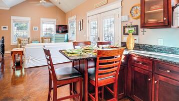 A kitchen with wooden cabinets, a dining table with chairs, and a large window with blinds.