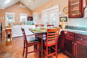 A kitchen with wooden cabinets, a dining table with chairs, and a large window with blinds. - Heart of Historic Chickamauga! Chic Studio w/ Pool (Chickamauga)