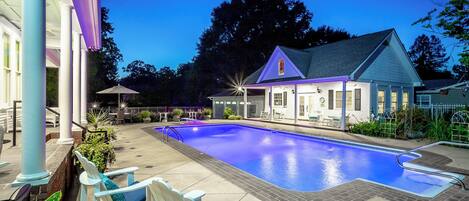 A swimming pool with lounge chairs, a covered patio, and a building with a gabled roof.