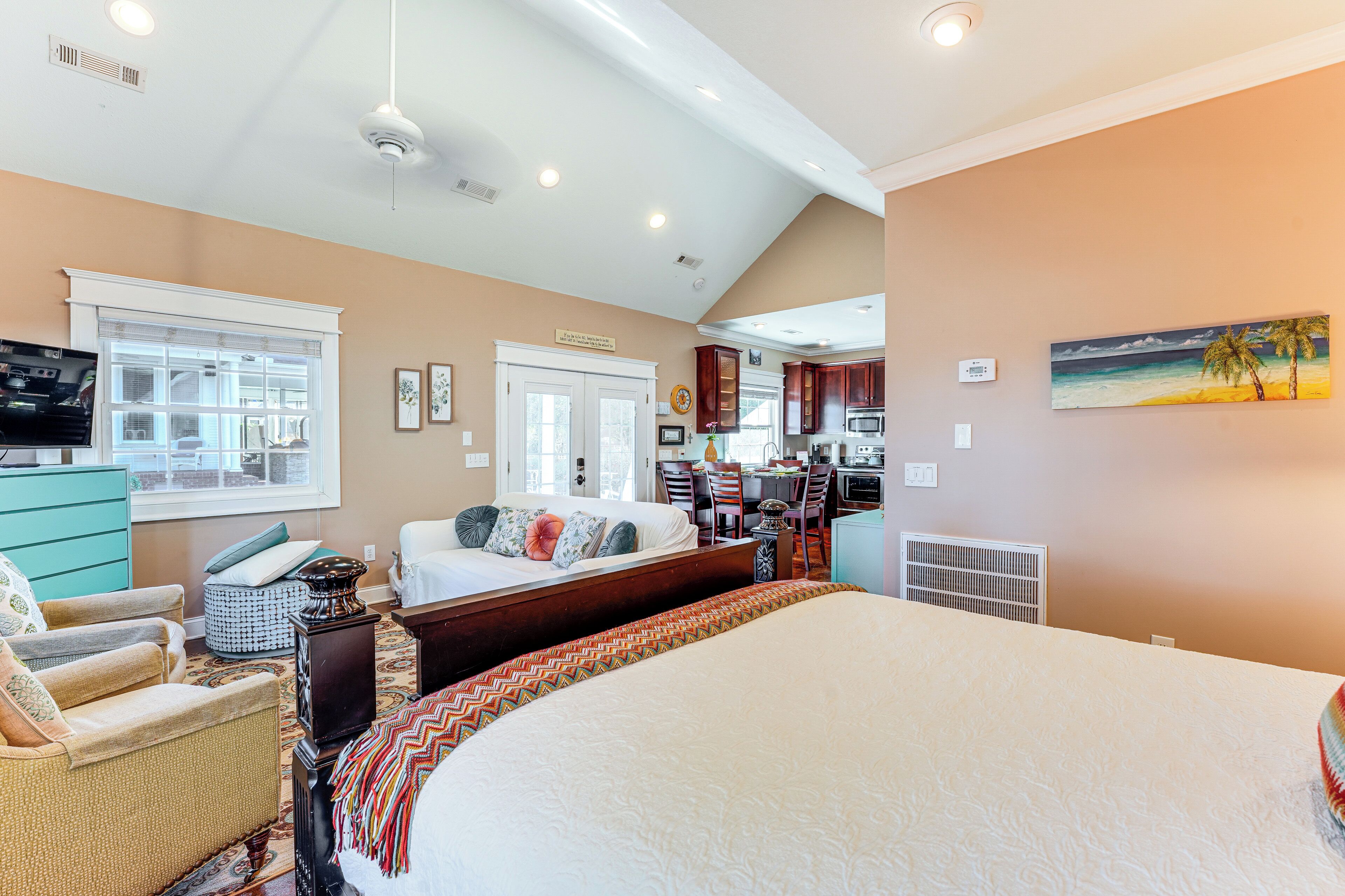 A spacious bedroom with a large bed, a sitting area with a sofa and chairs, a kitchen area, and a dining table.