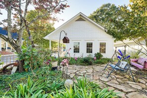 A white house with a stone pathway, a swing set, and a birdhouse in the garden.