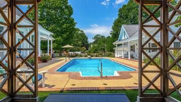 A pool area with a wooden pergola, a brick deck, and a view of surrounding houses.