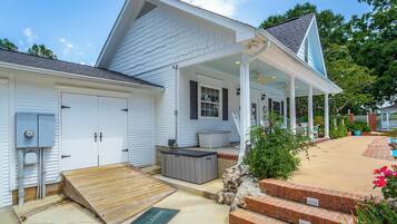 A white house with a covered porch, a small patio, and a wooden ramp leading to the entrance.