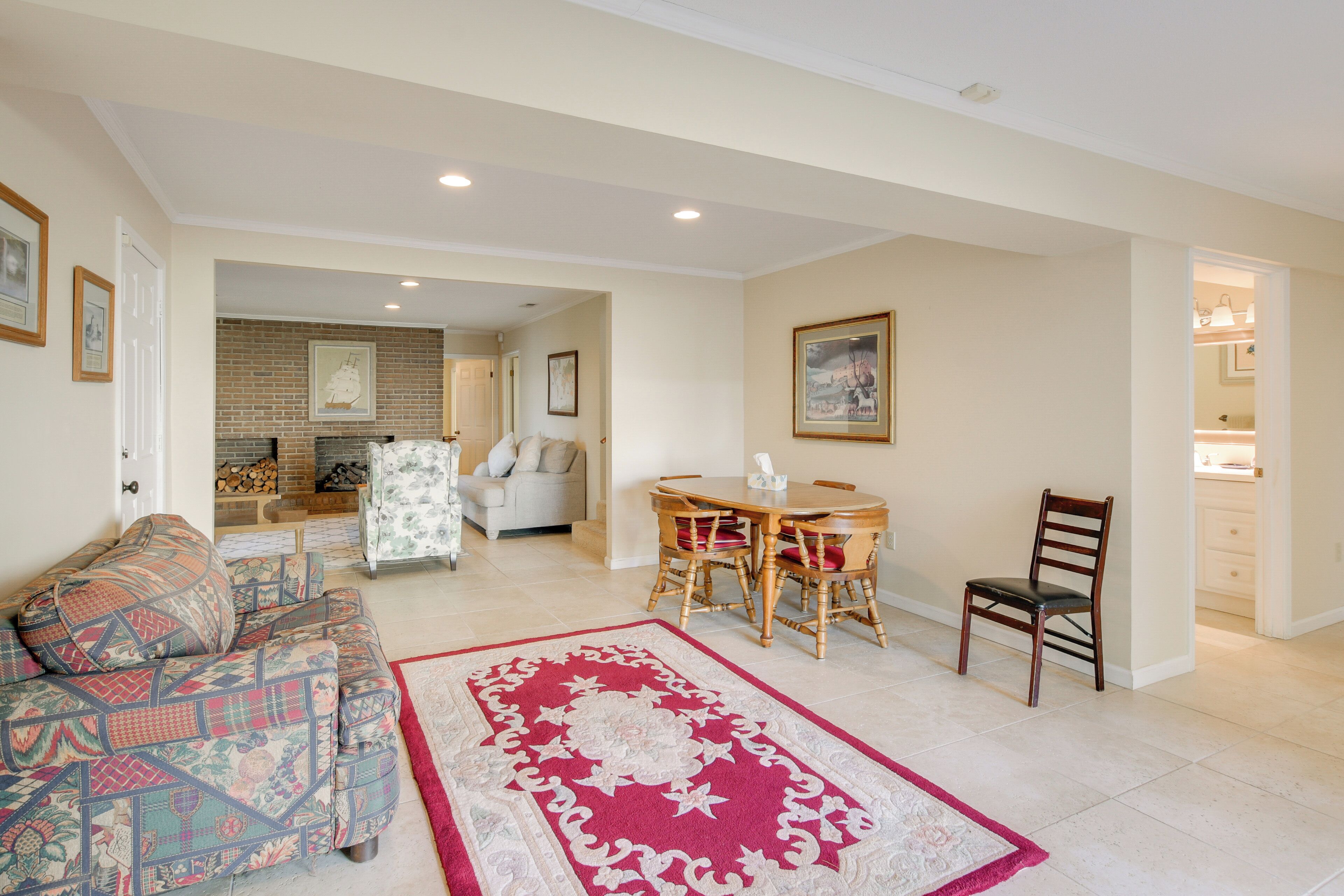 A spacious living room with a patterned sofa, a dining table with chairs, and a red and white rug.
