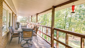 A covered patio with a table and chairs, a brick wall, and a view of trees.