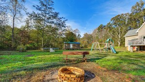 A backyard with a wooden fire pit, a picnic table, a swing set, and a small shed.