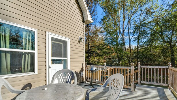 A covered outdoor deck with a table and chairs, a grill, and a wooden fence.