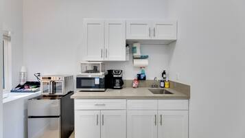 A compact kitchen with white cabinets, a microwave, a toaster, and a small refrigerator.