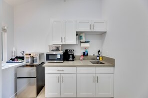 Cozinha compacta com armários brancos, micro-ondas, torradeira e pequena geladeira.
