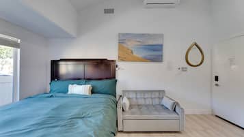 A bedroom with a bed, a sofa, an air conditioner, a painting, and a mirror on the wall.