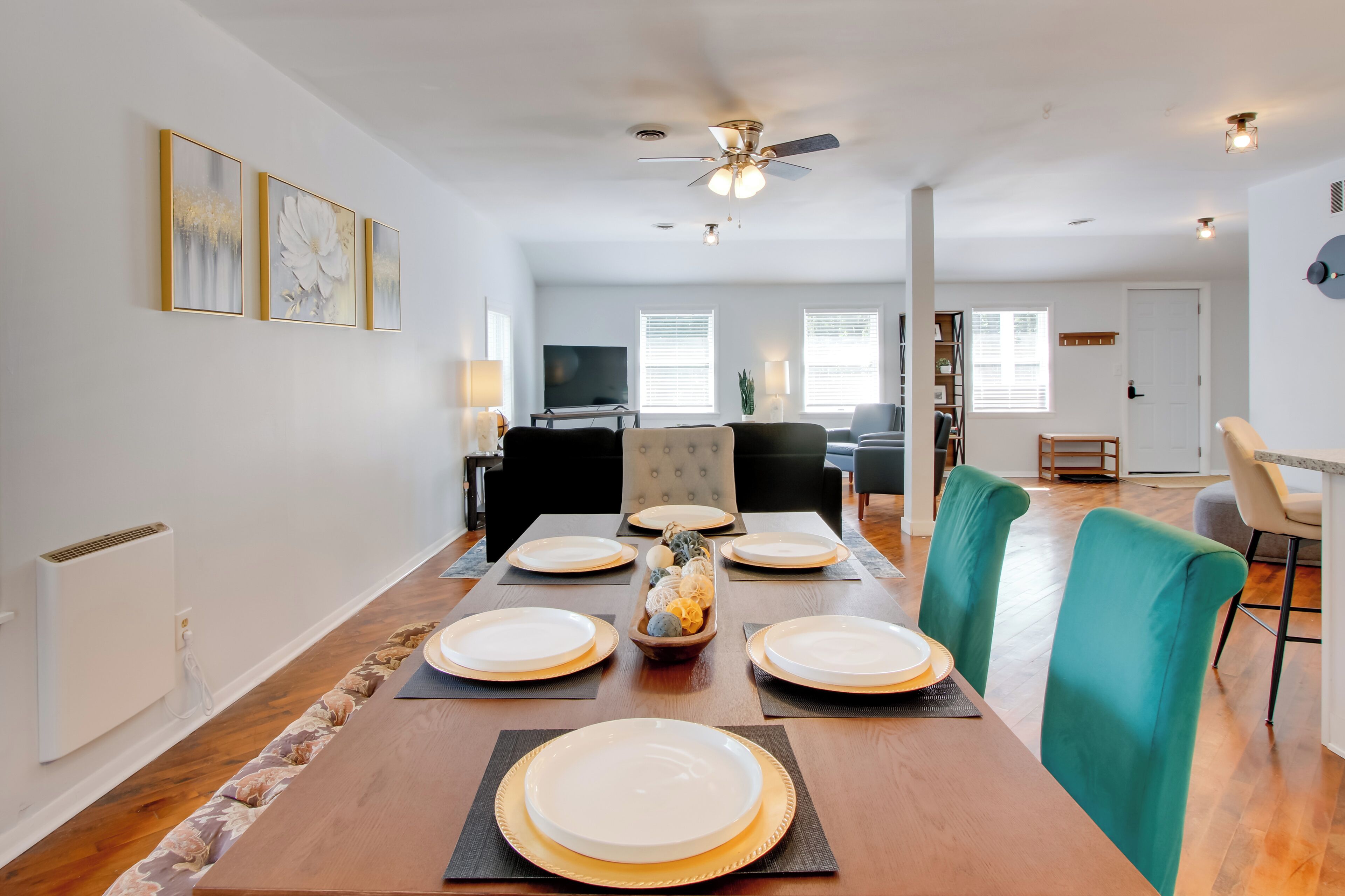 A dining area with a long wooden table set for four, surrounded by teal chairs, with a ceiling fan above.