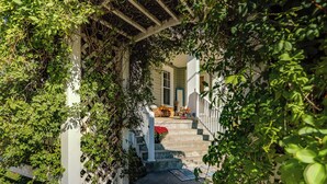 A covered outdoor staircase leading to a house entrance, surrounded by lush greenery.