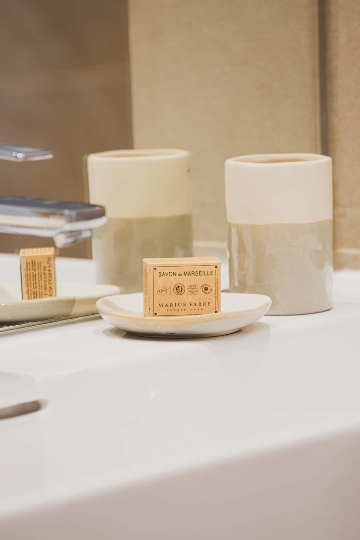 A bathroom with a white sink, a soap dish with a bar of soap, and two large bottles of soap.