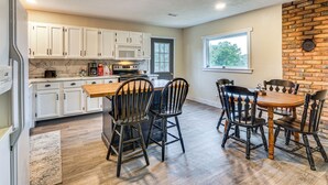 A kitchen with white cabinets, a wooden dining table, and black chairs. - Dog-friendly Cabin w/ Yard Near Auxvasse Creek! (Kingdom City)