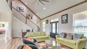 A spacious living room with a staircase, two green sofas, a glass coffee table, and a patterned rug. - Farm Animals On-site: Needville Ranch Getaway! (Needville)
