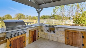 An outdoor kitchen with a grill, sink, and wooden cabinets. - Farm Animals On-site: Needville Ranch Getaway! (Needville)
