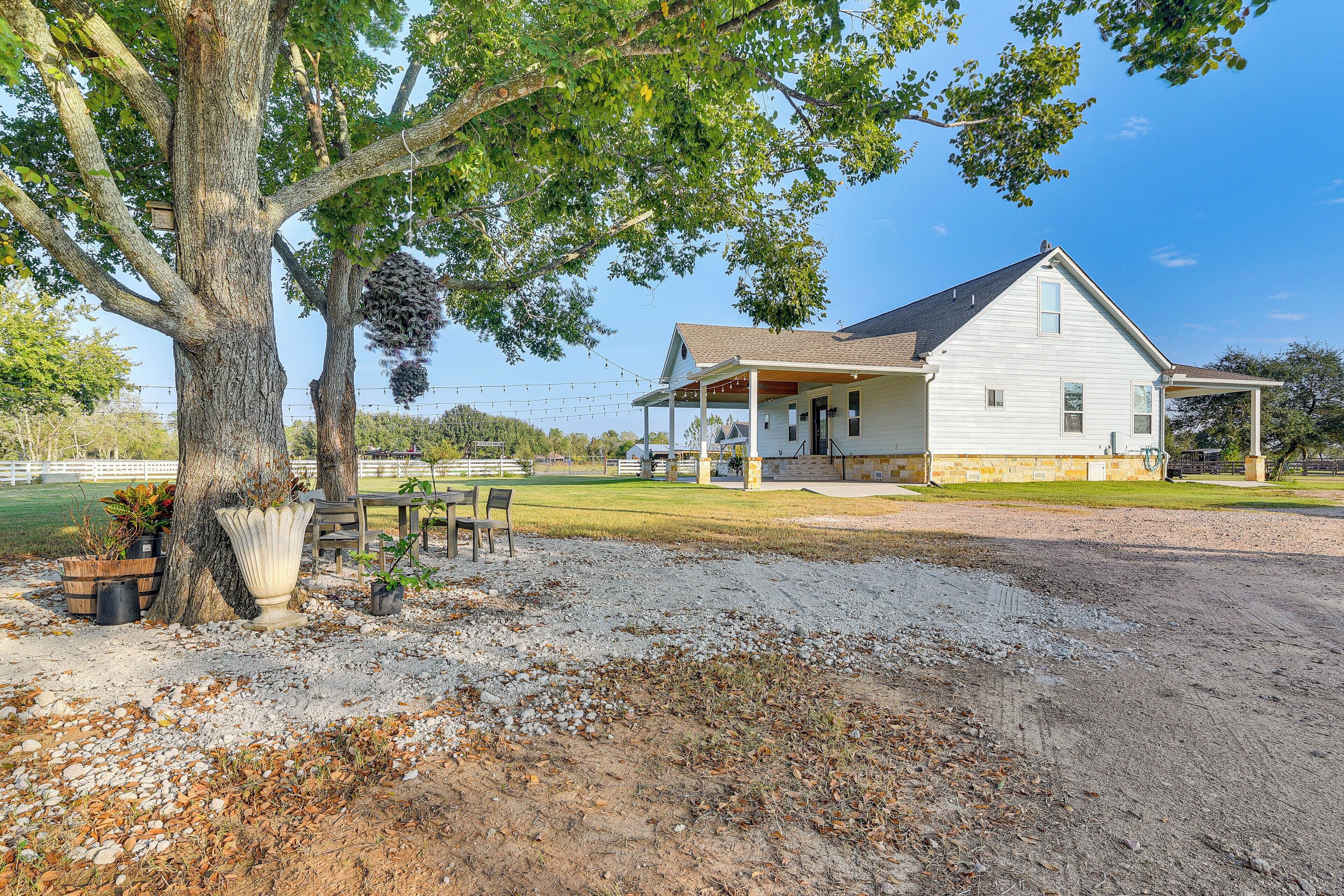 A white house with a porch, a large tree, and a gravel driveway.