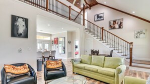 A spacious living room with a green sofa, two leather armchairs, and a glass coffee table. A staircase with wooden railings leads to an upper level. - Farm Animals On-site: Needville Ranch Getaway! (Needville)
