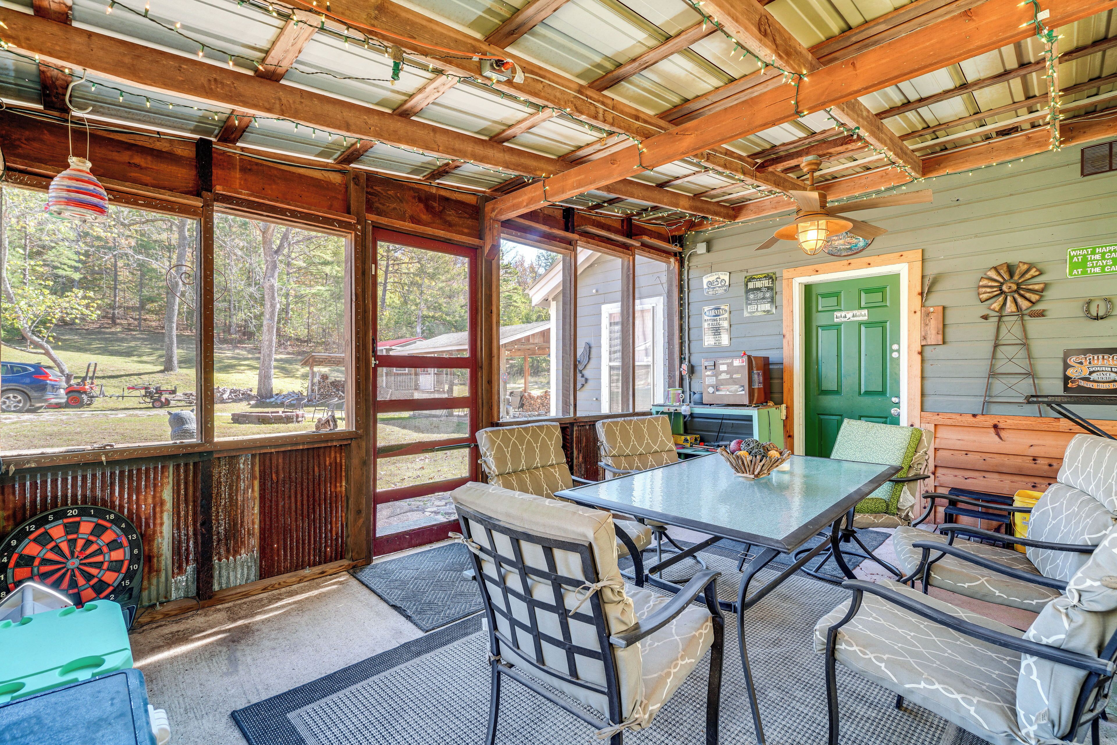 A rustic dining area with a table and chairs, large windows, and a green door.