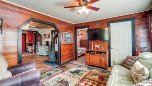 A cozy living room with a wooden floor, a ceiling fan, a sofa, a coffee table, and a fireplace. - Hunters/floaters Welcome! Creekside Missouri Cabin (Annapolis)