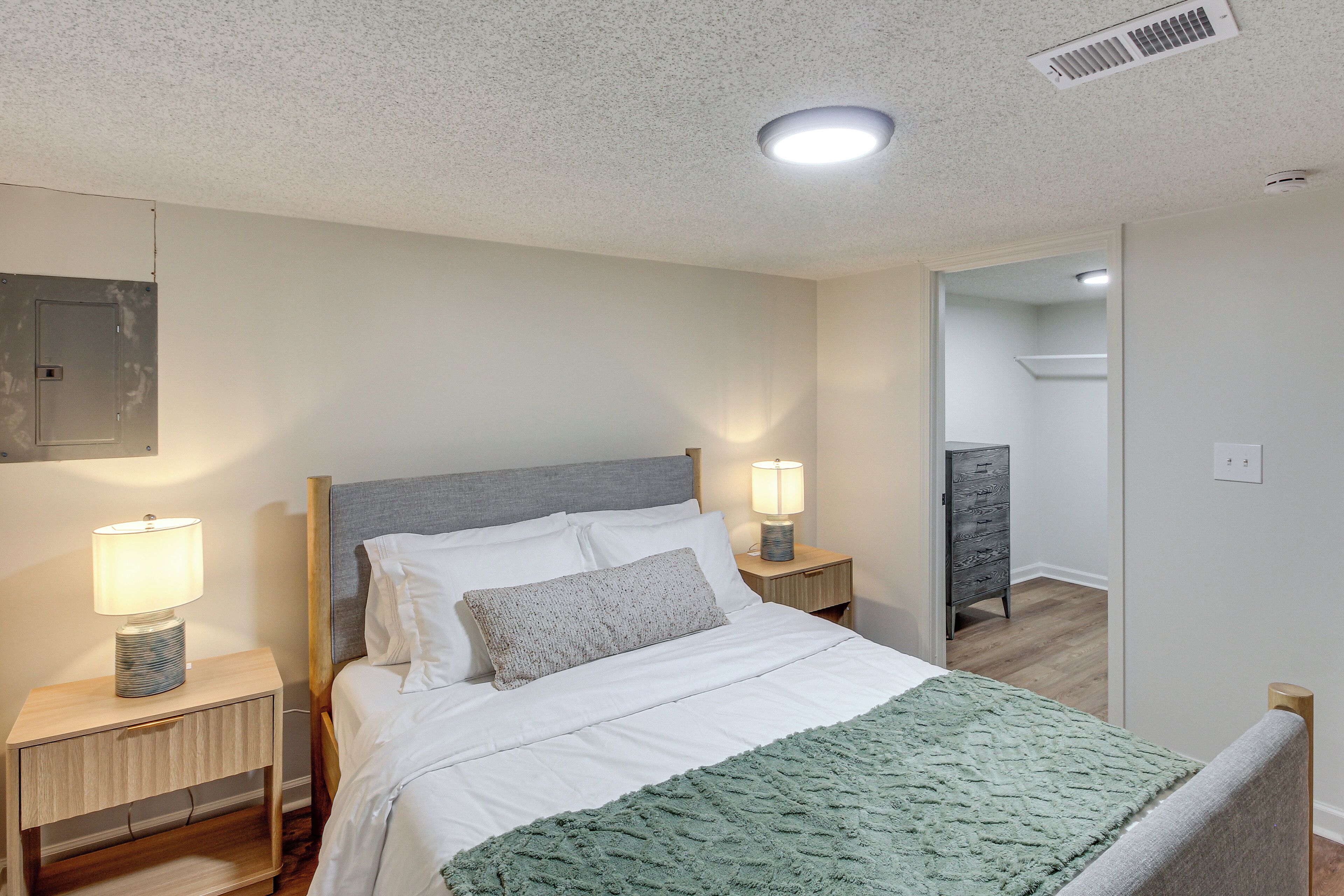 A neatly made bed with a grey headboard, two bedside lamps, and a green throw blanket.