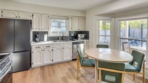 A modern kitchen with white cabinets, stainless steel appliances, and a dining area with a round table and chairs. - 19 Mi to Kansas City: Group Retreat w/ Game Room! (Blue Springs)