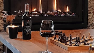 A fireplace with a stone wall backdrop, a bottle of wine, a glass of red wine, a chessboard, and a wooden bar counter.