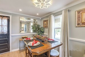Un coin repas avec une table en bois dressée pour quatre personnes, un grand miroir et une plante en pot.