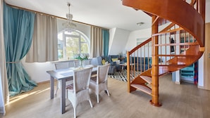 A dining area with a table and chairs, a chandelier, and a view of the outdoors through large windows. - Apartamenty Świnoujście - Trzy Korony (Świnoujście)