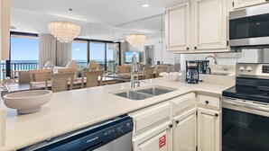 A modern kitchen with a dishwasher, a stove, and a sink. There is a dining area with chairs and a table. - Gulf Front - Unsurpassable Views - Pool - Workout Room - Private Beach Access (Santa Rosa Beach)