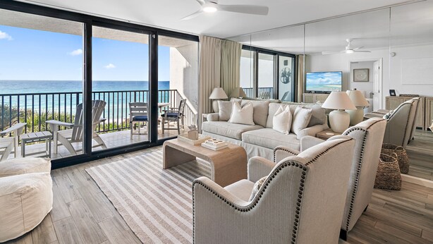 A spacious living room with a large sofa, armchairs, and a coffee table. A television is mounted on the wall, and the room has a balcony with a view of the ocean. - Gulf Front - Unsurpassable Views - Pool - Workout Room - Private Beach Access (Santa Rosa Beach)