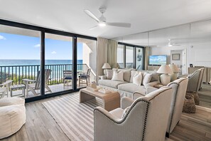 A spacious living room with a large sofa, armchairs, and a coffee table. A television is mounted on the wall, and the room has a balcony with a view of the ocean. - Gulf Front - Unsurpassable Views - Pool - Workout Room - Private Beach Access (Santa Rosa Beach)