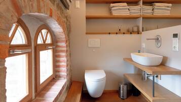 Un baño con inodoro blanco, tocador de madera con lavamanos y un perchero encima.
