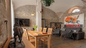A rustic dining area with a wooden table, chairs, and a horse sculpture centerpiece. There is a stone wall and a mural depicting a horse race. - Ab 1 Person: Rittergut mit Kamin, Fasssauna und mehr Nähe Sächsische Schweiz Dresden (Großharthau)